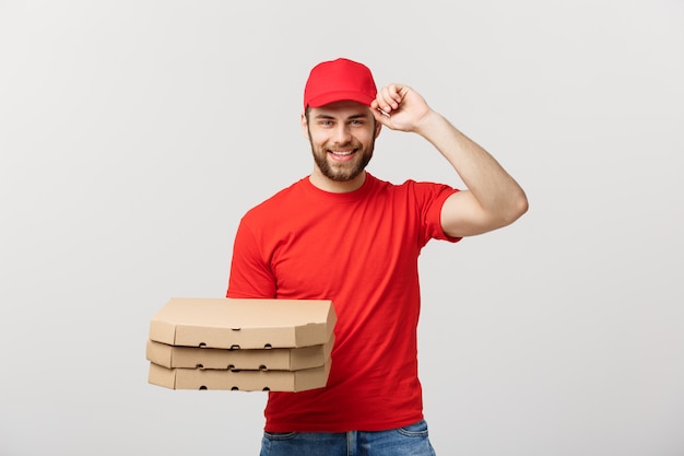 Mensajero hermoso del hombre de entrega de la pizza en uniforme rojo con la tapa que sostiene las cajas de la pizza. Aislado