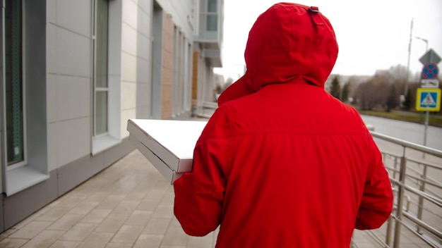 Un mensajero de hombre vestido de rojo entregando pizza caminando por la calle