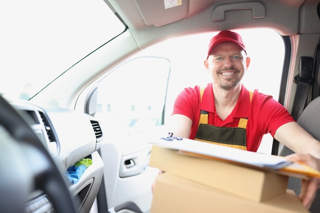 Mensajero macho sonriente saca la caja de cartón del coche