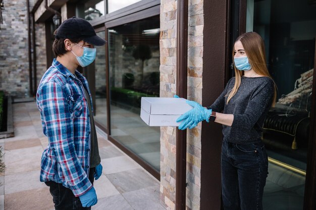 Mensajero con máscara protectora y guantes médicos entrega comida para llevar Servicio de entrega en condiciones de pandemia de brote de enfermedad de cuarentena coronavirus covid19