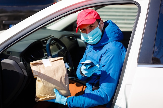 Mensajero con máscara protectora y guantes médicos entrega comida para llevar. Servicio de entrega en cuarentena, brote de enfermedad, condiciones de pandemia de coronavirus covid-19.