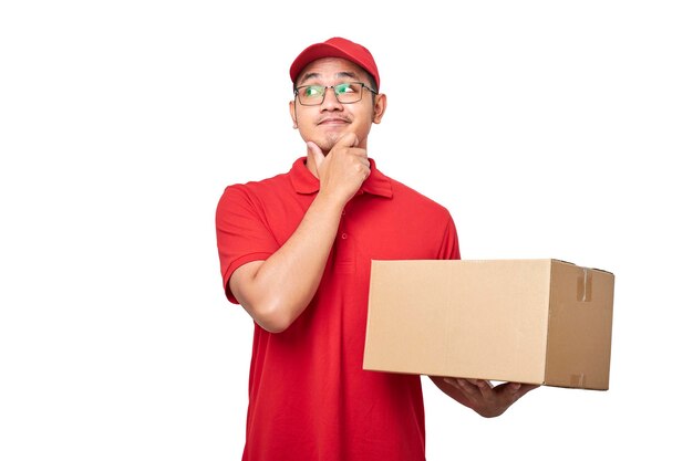 Foto mensajero masculino asiático joven pensativo en uniforme rojo que sostiene la caja con el pedido del cliente y pensando mirando la esquina superior izquierda