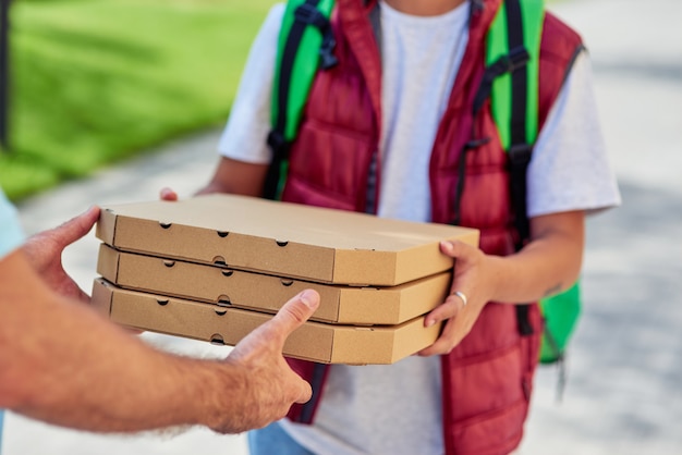 Mensajero masculino dando cajas con pizza al cliente mientras está de pie en una calle soleada