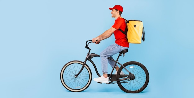 Mensajero masculino montando bicicleta posando con mochila bolsa fondo azul