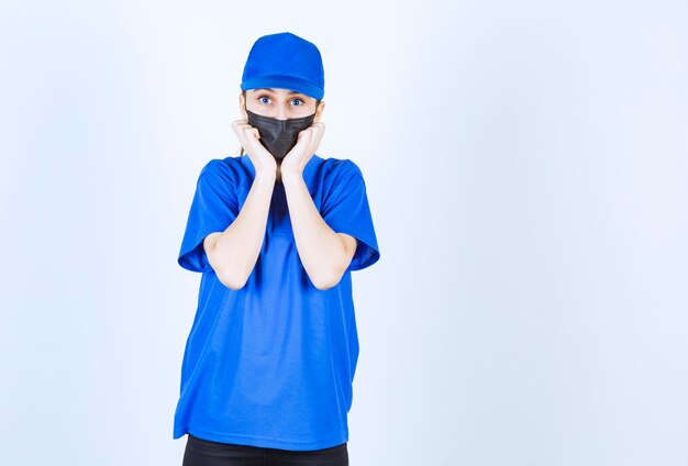 Mensajero mujer con máscara y uniforme azul parece asustada y aterrorizada.