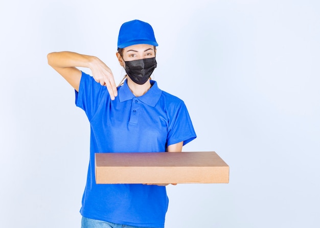 Mensajero mujer en uniforme azul y mascarilla entregando una caja de cartón al cliente.