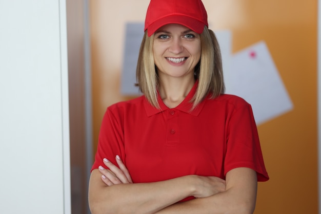 Mensajero de mujer en uniforme está de pie y sonriendo con los brazos cruzados