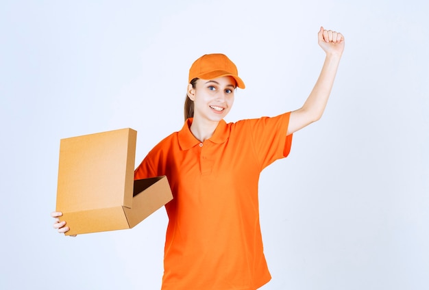 Mensajero mujer en uniforme naranja sosteniendo una caja de cartón abierta y mostrando su puño.