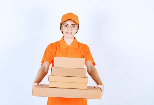 Mensajero mujer en uniforme naranja sosteniendo un stock de paquetes de cartón