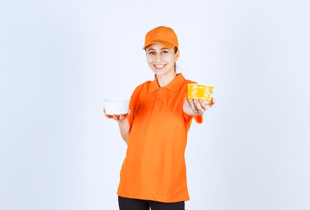 Mensajero mujer en uniforme naranja con taza de fideos de plástico y amarillo en ambas manos.