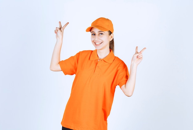 Foto mensajero mujer vistiendo uniforme naranja y gorra mostrando el signo de la paz.