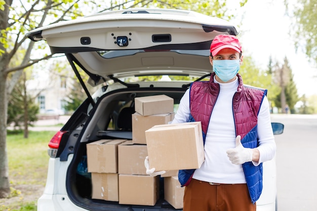 El mensajero, repartidor con guantes de látex médico y máscara, entrega de forma segura las compras en línea en una caja blanca a la puerta durante la epidemia de coronavirus, COVID-19. Quédate en casa, concepto seguro.