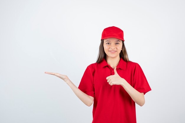 mensajero de sexo femenino joven en uniforme rojo que da los pulgares para arriba.