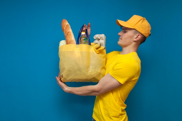 Mensajero en uniforme amarillo sosteniendo una bolsa ecológica de tela llena de comida y sonriendo