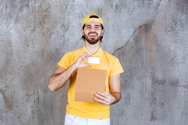 Mensajero en uniforme amarillo sosteniendo una caja de cartón abierta y presentando una tarjeta de visita