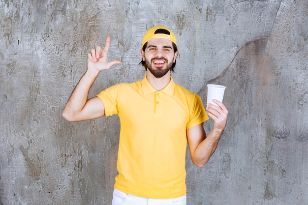 Mensajero en uniforme amarillo sosteniendo un vaso desechable y pensando o teniendo una buena idea.