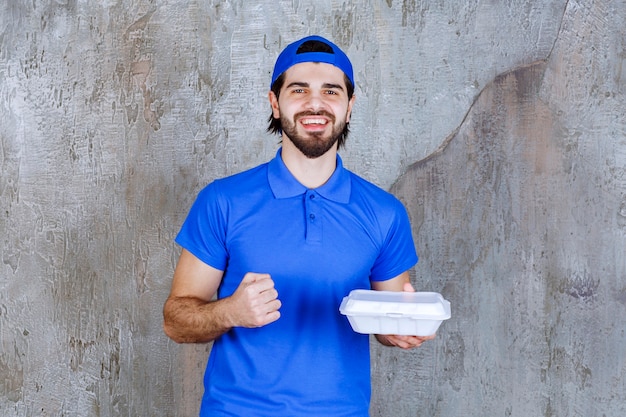 Mensajero en uniforme azul sosteniendo una caja de comida para llevar de plástico y mostrando su puño