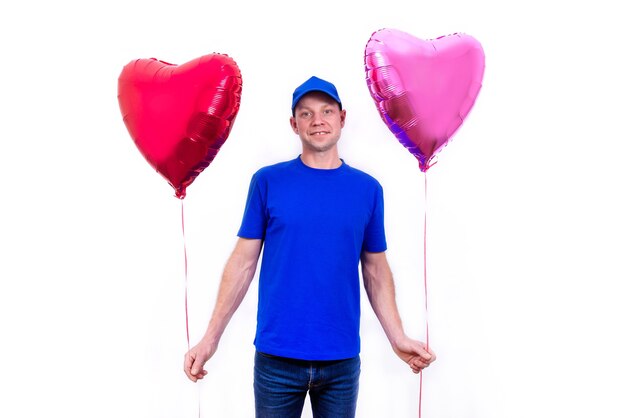 Mensajero con uniforme azul sostiene una caja de regalo roja en forma de corazón y un globo para el Día de San Valentín.