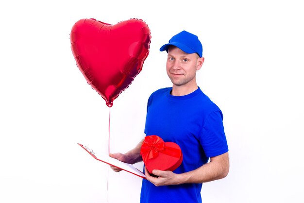 Mensajero en uniforme azul sostiene una caja de regalo roja en forma de corazón y un globo para el Día de San Valentín