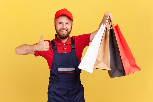 Mensajero en uniforme sosteniendo bolsas de compras en la mano mostrando el pulgar hacia arriba entrega rápida de la tienda