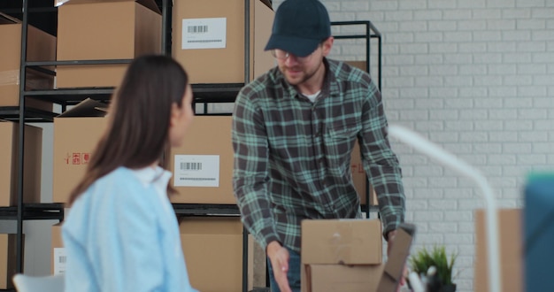 El mensajero viene a recoger el paquete para el cliente Gerente femenina usando una computadora portátil preparando el paquete para la entrega postal