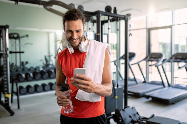 Mensajes de texto de deportista feliz en el teléfono móvil en un club de salud
