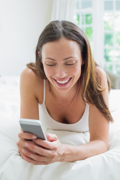 Mensajes de texto sonrientes de la mujer en cama