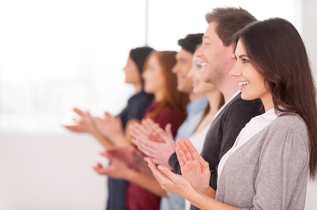 Menschen applaudieren. Seitenansicht einer Gruppe fröhlicher junger Leute, die in einer Reihe stehen und jemandem applaudieren