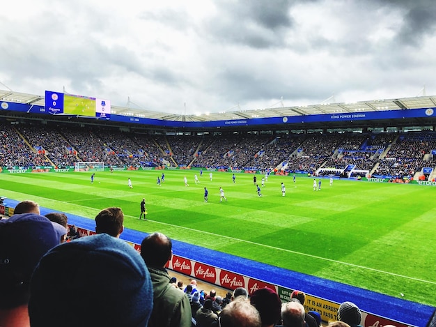 Menschen beobachten ein Fußballspiel im Stadion gegen den Himmel