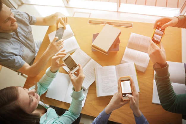 Foto menschen, bildung, technologie und prüfungskonzept - nahaufnahme von schülern mit smartphones, die bilder von buchseiten machen und in der schulbibliothek einen spickzettel erstellen