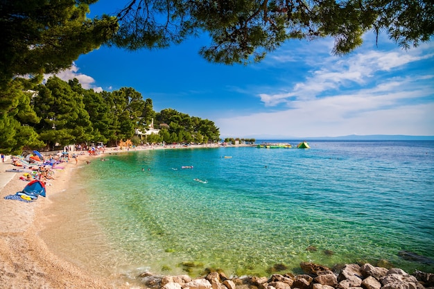 Menschen, die auf einem kleinen Kieselstrand in Brela, Makarska Riviera, Kroatien schwimmen und sich sonnen