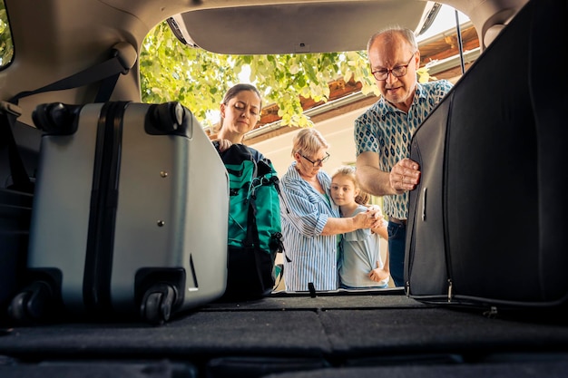 Menschen, die Koffer und Gepäck in den Kofferraum laden und sich auf die Sommerferienreise vorbereiten. Kleines Kind und Familie, die mit dem Fahrzeug in den Urlaub fahren, mit den Großeltern auf Abenteuer gehen.