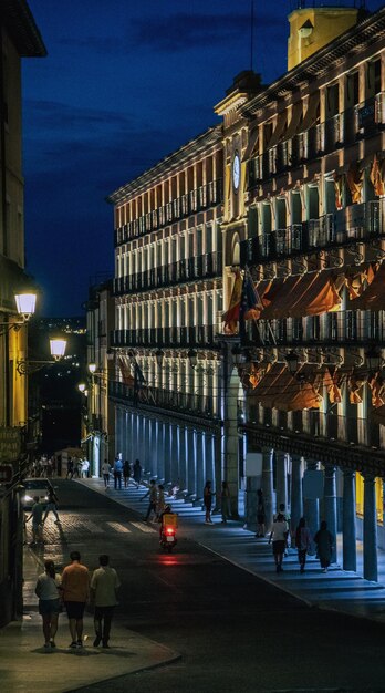 Menschen, die nachts auf einer Straße in Toledo spazieren gehen, die wunderschön von Straßenlaternengeschäften beleuchtet wird