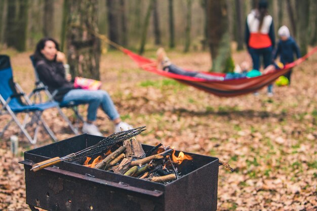 Menschen, die sich im Freien ausruhen, grillen mit Feuer in der Nähe einer Hängematte im Hintergrund