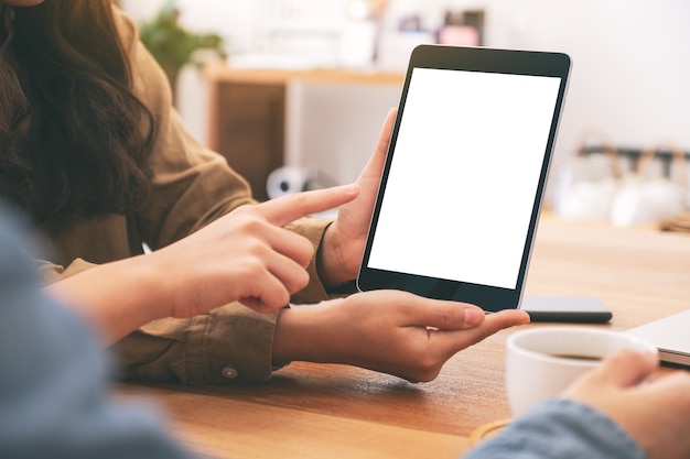 Menschen, die zusammen denselben Mockup-Tablet-PC auf einem Holztisch verwenden, betrachten und darauf zeigen