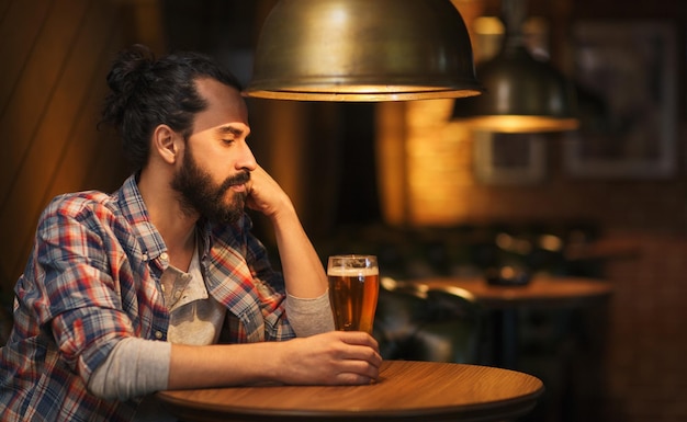 menschen, einsamkeit, alkohol und lifestyle-konzept - unglücklicher alleinstehender mann mit bart, der bier in der bar oder im pub trinkt