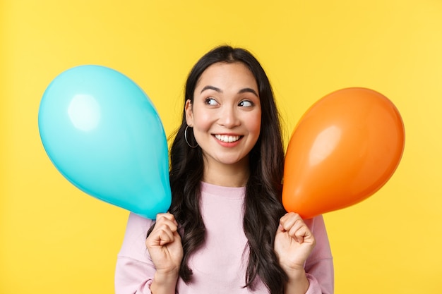 Menschen Emotionen, Lifestyle-Freizeit- und Schönheitskonzept. Schönes verträumtes asiatisches Mädchen mit zwei Ballons, die in der oberen linken Ecke aufgeregt und fasziniert aussehen, fröhlich lächeln, sich viele Geschenke vorstellen.