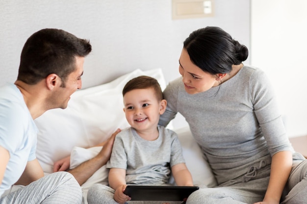 Menschen-, Familien- und Technologiekonzept - glückliche Mutter, Vater und kleiner Junge mit Tablet-PC-Computer im Bett zu Hause oder im Hotelzimmer