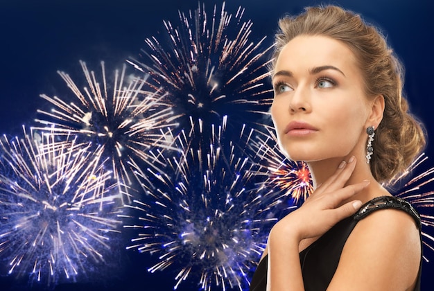 Menschen, Feiertage und Glamour-Konzept - schöne Frau mit Ohrringen über Feuerwerk auf dunkelblauem Hintergrund