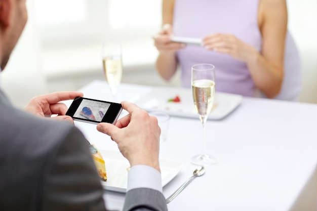 Menschen, Freizeit, Essen und Technologiekonzept - Nahaufnahme eines Paares mit Smartphones, das Essen im Restaurant fotografiert