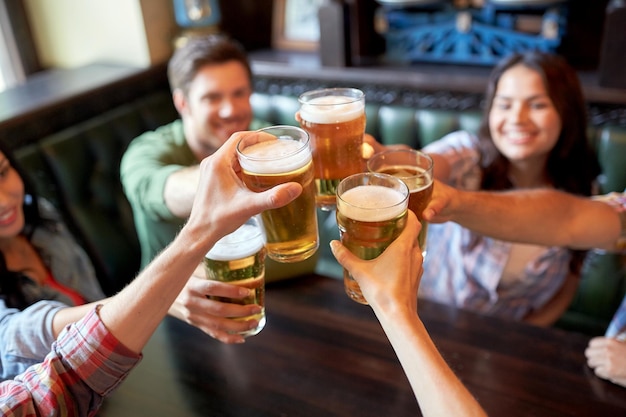 Foto menschen, freizeit, freundschaft und feierkonzept - glückliche freunde trinken fassbier und klirren mit gläsern in der bar oder im pub