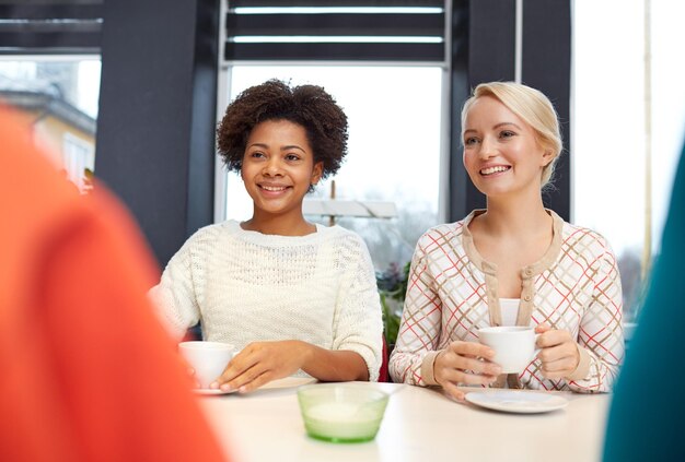 menschen, freizeit, freundschaft und kommunikationskonzept - glückliche junge frauen treffen sich und trinken tee oder kaffee im café