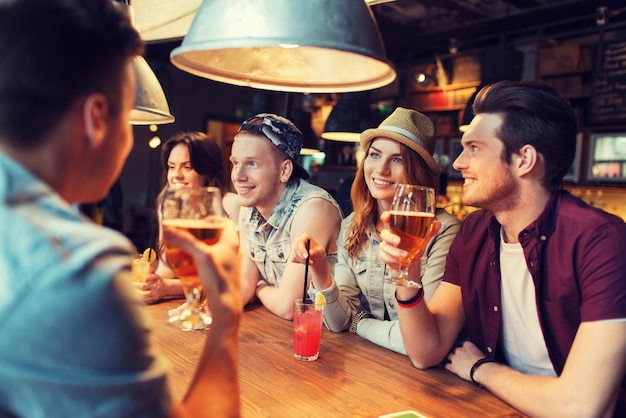 menschen-, freizeit-, freundschafts- und kommunikationskonzept - gruppe glücklich lächelnder freunde, die bier und cocktails trinken und in der bar oder im pub sprechen