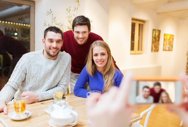 menschen-, freizeit-, freundschafts- und technologiekonzept - gruppe glücklicher freunde mit smartphone, die fotos machen und tee im café trinken