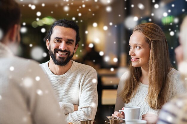 menschen, freizeit, kommunikation, saison und konzept - glückliche freunde treffen sich und trinken tee oder kaffee im wintercafé