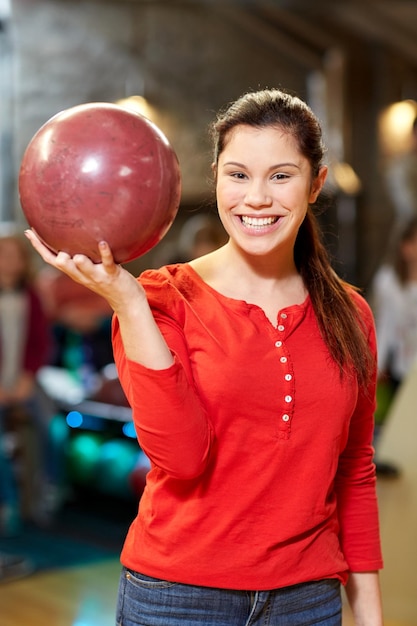 menschen-, freizeit-, sport- und unterhaltungskonzept - glückliche junge frau, die ball im bowlingclub hält