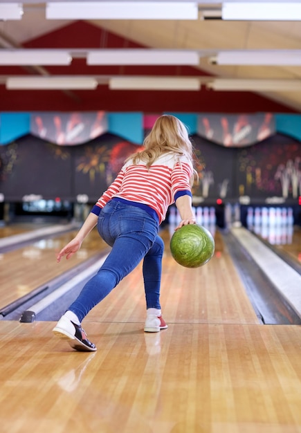 menschen-, freizeit-, sport- und unterhaltungskonzept - glückliche junge frau, die ball im bowlingclub wirft