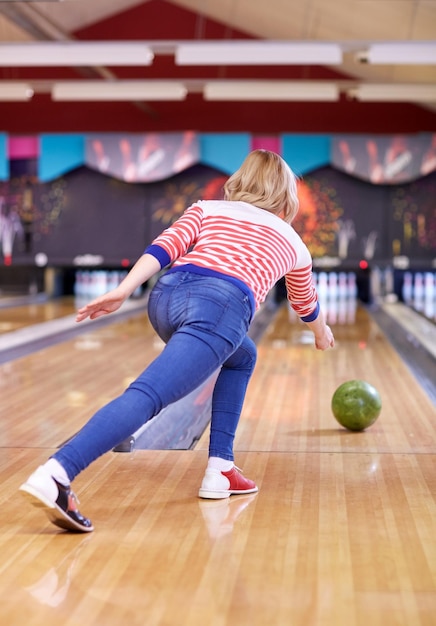 menschen-, freizeit-, sport- und unterhaltungskonzept - glückliche junge frau, die ball im bowlingclub wirft