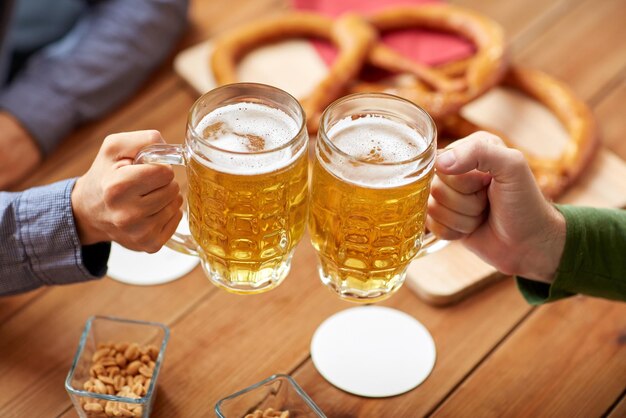 Foto menschen-, freizeit- und getränkekonzept - nahaufnahme männlicher hände, die bierkrüge und brezeln in der bar oder im pub klirren