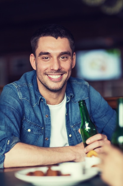 menschen-, freizeit- und junggesellenabschiedskonzept - glücklicher junger mann, der bier in der bar oder im pub trinkt